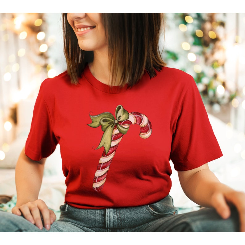 May include: Red t-shirt with a white and red candy cane with a green bow on top.