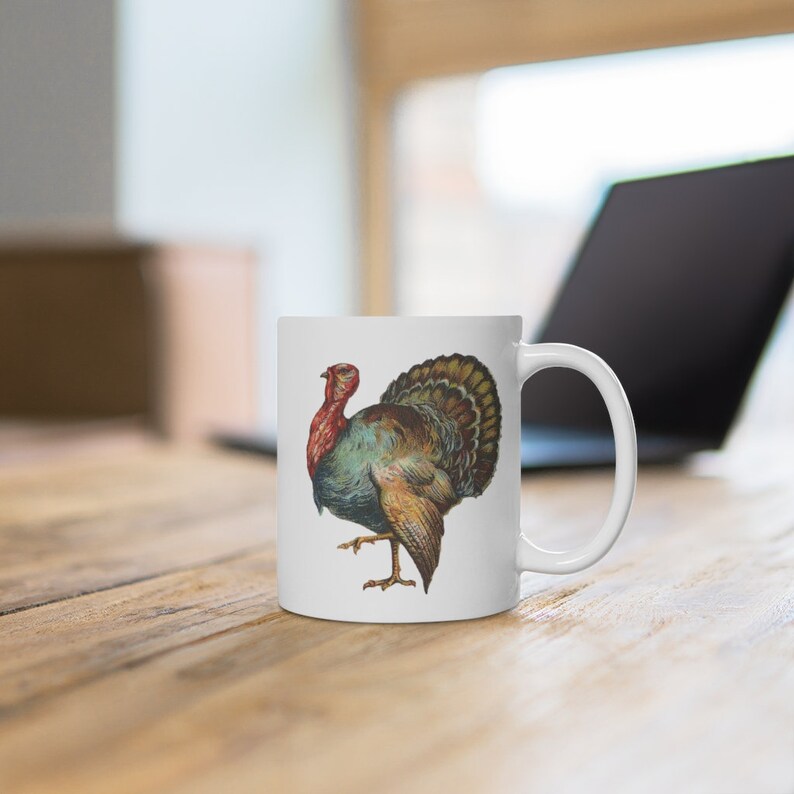 Puede incluir: Taza de cer&aacute;mica blanca con una ilustraci&oacute;n colorida de un pavo. El pavo tiene la cabeza roja, el cuerpo azul y las plumas marrones y verdes.