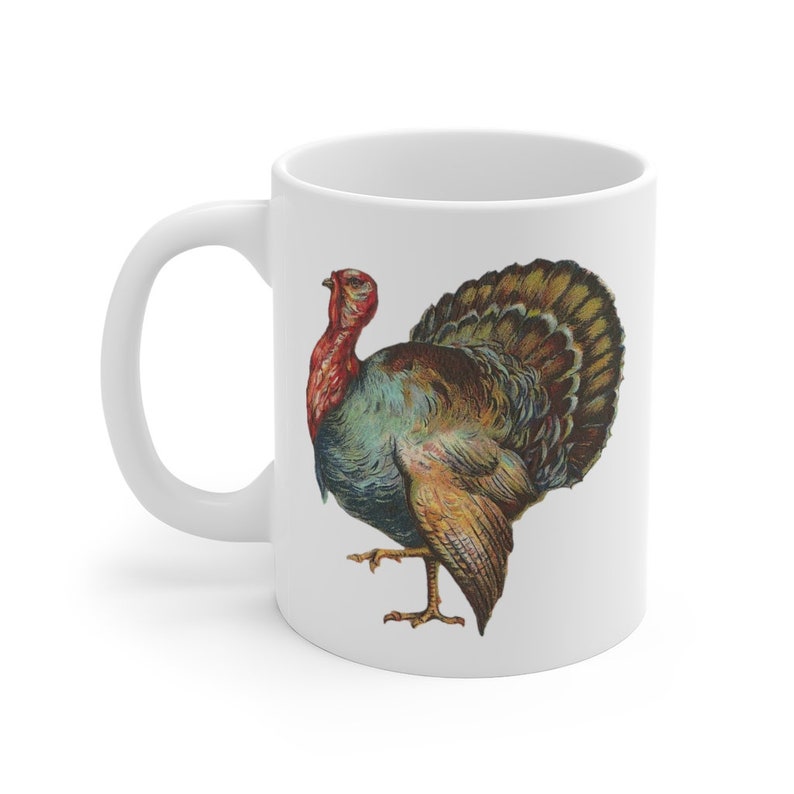 Puede incluir: Taza de cer&aacute;mica blanca con una ilustraci&oacute;n colorida de un pavo. El pavo tiene la cabeza roja, plumas azules y verdes y plumas de cola marrones y doradas.