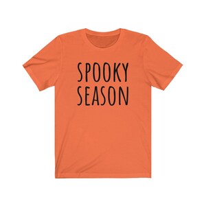 May include: Orange short-sleeved t-shirt with the text "SPOOKY SEASON" printed in black.