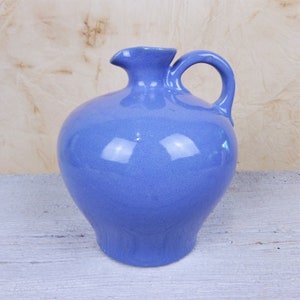 May include: A light blue ceramic pitcher with a rounded body and a handle. The pitcher has a smooth, glossy finish.