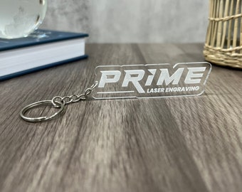 May include: A clear acrylic keychain with the word "PRIME" and the text "LASER ENGRAVING" in white lettering.