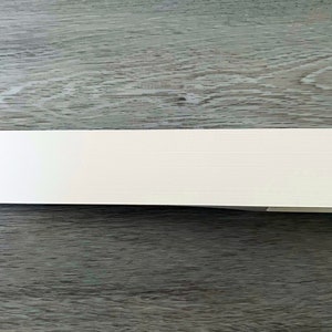 Puede incluir: Una pila de tarjetas blancas plegadas con una superficie texturizada. Las tarjetas son rectangulares y parecen estar en blanco, descansando sobre una superficie de madera gris. Las tarjetas son probablemente para invitaciones o notas.