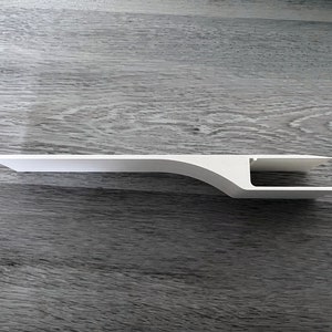 Puede incluir: Una estanter&iacute;a blanca de estilo moderno con un dise&ntilde;o curvo &uacute;nico. La estanter&iacute;a tiene una parte superior plana y rectangular y un soporte curvo, con un recorte rectangular en el extremo. La estanter&iacute;a est&aacute; hecha de un material s&oacute;lido y opaco.