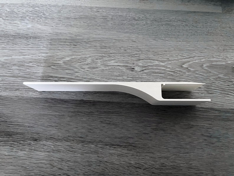 Puede incluir: Una estanter&iacute;a blanca de estilo moderno con un dise&ntilde;o curvo &uacute;nico. La estanter&iacute;a tiene una parte superior plana y rectangular y un soporte curvo, con un recorte rectangular en el extremo. La estanter&iacute;a est&aacute; hecha de un material s&oacute;lido y opaco.