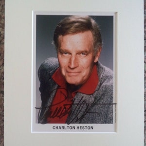 Op de afbeelding: Een zwart-witfoto van Charlton Heston, een beroemde acteur, met zijn handtekening onder de foto.