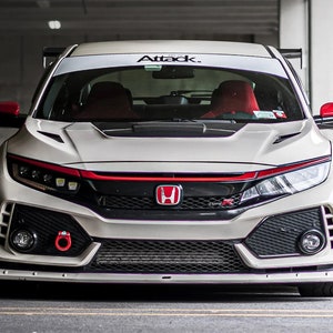 May include: A white Honda Civic Type R with red accents, a black front grille, and a black hood. The car has a white windshield banner with the text "Attack." The car is parked in a garage.