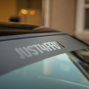 Puede incluir: Un coche negro con una pancarta gris en el parabrisas que dice "JUST4FFU".