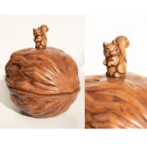 Puede incluir: Un cascanueces de cerámica con forma de nuez con una figurita de ardilla en la parte superior. El cascanueces es marrón y tiene una textura detallada.