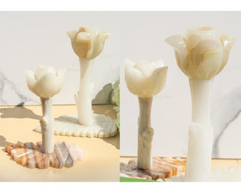 May include: Two white marble flower sculptures with intricate details. Each flower sits on a leaf-shaped base made of brown and white marble.