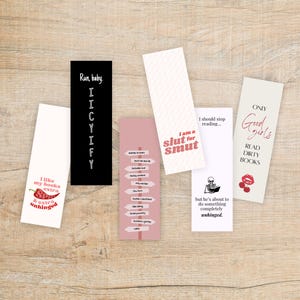 May include: A collection of rectangular bookmarks with various designs and text. One bookmark is black with white text, another is white with a red chili pepper graphic, and others have phrases like "I am a slut for smut" and "Read dirty books."