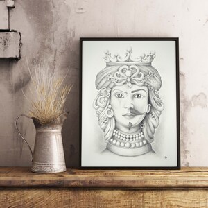 May include: A framed pencil drawing of a regal figure with a crown, half-woman and half-man, with ornate jewelry and a mustache. The artwork is displayed on a wooden shelf next to a metal jug with dried grass.
