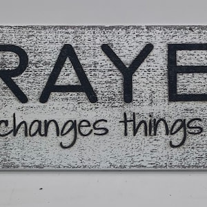May include: White wooden sign with black lettering that reads "PRAYER changes things".