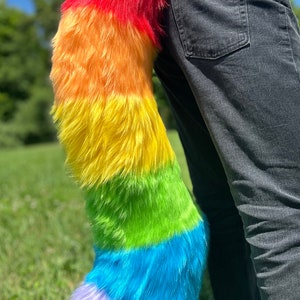 May include: A rainbow colored fluffy tail with red, orange, yellow, green, blue, and purple stripes. The tail is attached to a person's waist.