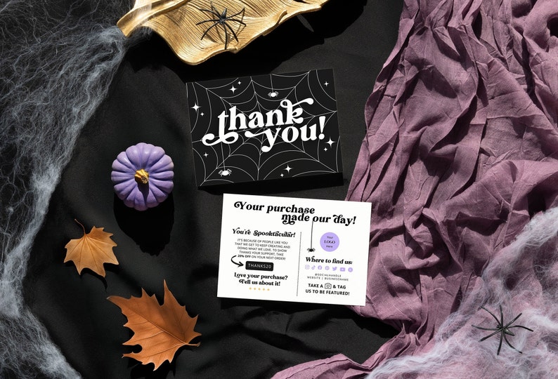 May include: A thank you card with a black and white spiderweb design and the text "thank you!" in white. The card is surrounded by purple fabric, brown leaves, and white spiderwebs.