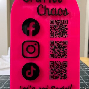 May include: Pink acrylic sign with the text "CraftTee Chaos" and the social media icons for Facebook, Instagram, and TikTok.  The sign also includes three QR codes and the text "Let's get Social!"