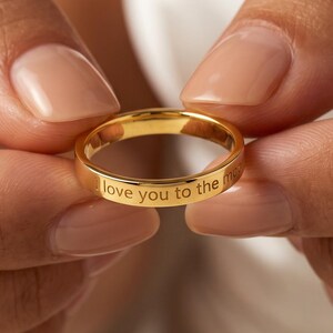 Peut inclure: Une bague anneau en métal doré poli avec une surface extérieure lisse et arrondie. Le métal est gravé avec le texte I love you to the moon, qui est clairement visible le long de la circonférence extérieure de ce bijou circulaire.