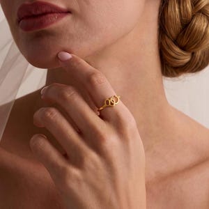 Puede incluir: Un anillo de oro que presenta una serie de tres formas de corazón caladas e interconectadas a lo largo de la banda. El anillo tiene un acabado liso y pulido, y se lleva en un dedo, mostrando el delicado trabajo en metal y el diseño.
