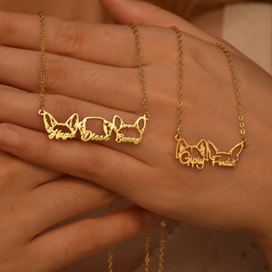 Peut inclure: Deux colliers en or avec des silhouettes de chiens et des noms. Le collier du haut porte les noms "Hops", "Diesel" et "Sunny". Le collier du bas porte les noms "Gipsy" et "Finnick".