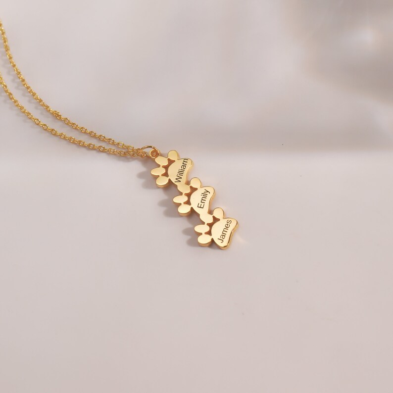 May include: Gold necklace with a paw print charm engraved with the names "William", "Emily", and "James".