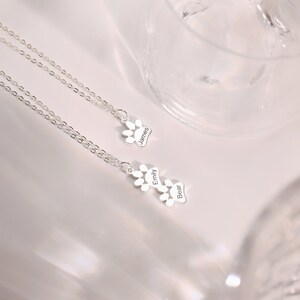 May include: Two silver necklaces with paw print charms. The charms are engraved with the names "James", "Emily", and "Bear".