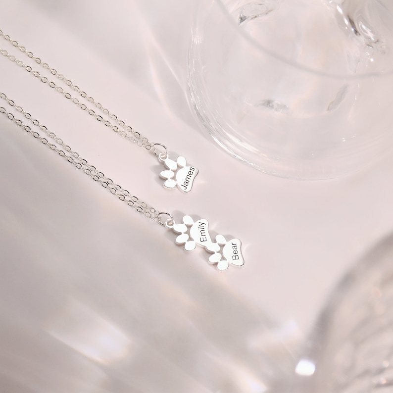 May include: Two silver necklaces with paw print charms. The charms are engraved with the names "James", "Emily", and "Bear".