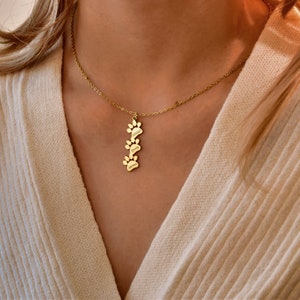 May include: Gold necklace with a charm of four paw prints, each with a name engraved on it: Dawson, Emily, and James.