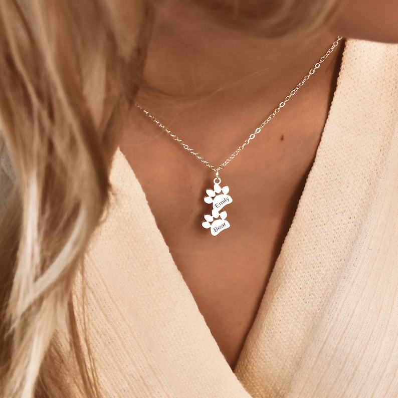 May include: Silver necklace with a double paw print charm. The charm is engraved with the names "Emily" and "Bear".