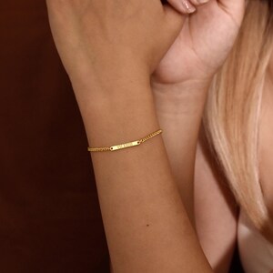 May include: A gold-toned chain bracelet featuring a central rectangular bar charm. The bar is engraved with the Roman numerals VII XXIII. The bracelet consists of a delicate link chain that secures around the wrist with a polished metallic finish.