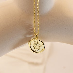 May include: Gold necklace with a paw print charm and the name "Bella" engraved on it.