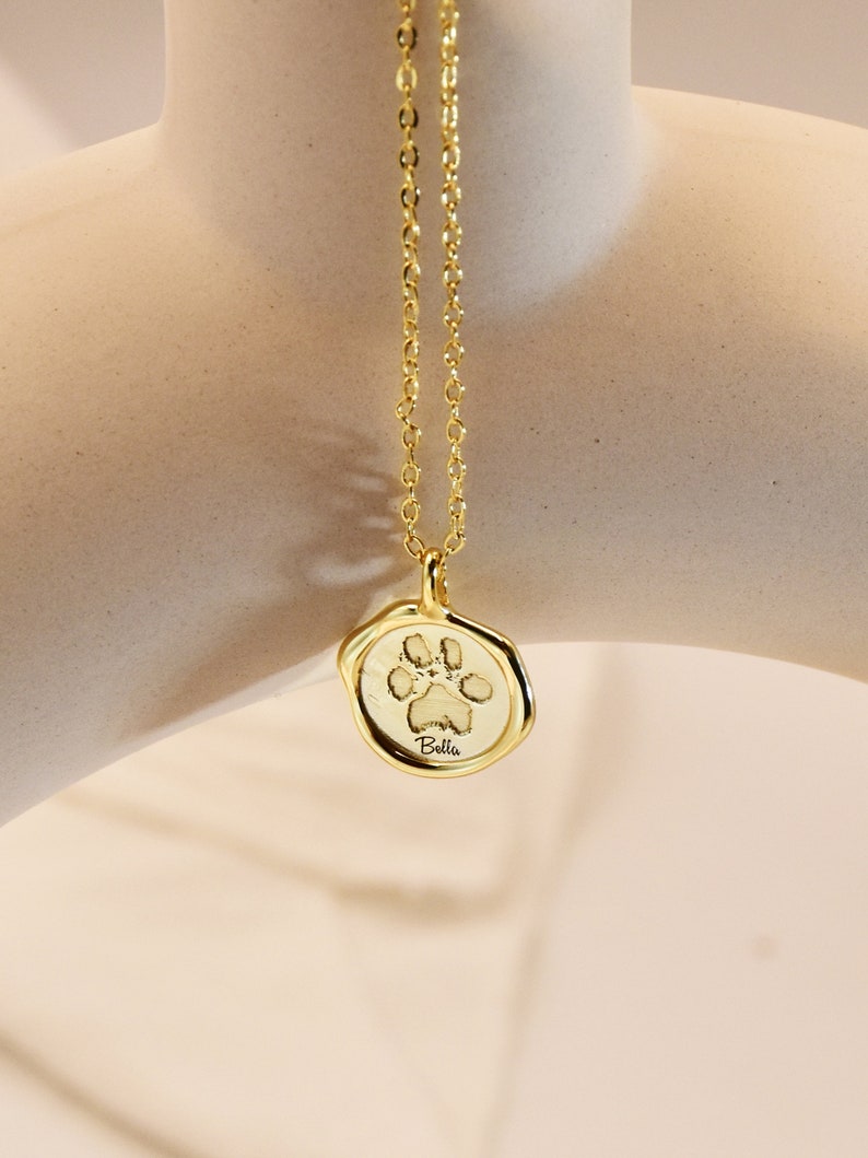 May include: Gold necklace with a paw print charm and the name "Bella" engraved on it.