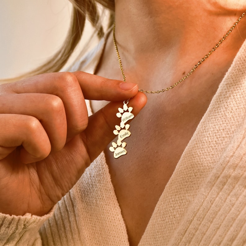 May include: Gold necklace with a pendant featuring four paw prints with the names William, Emily, and James engraved on them.