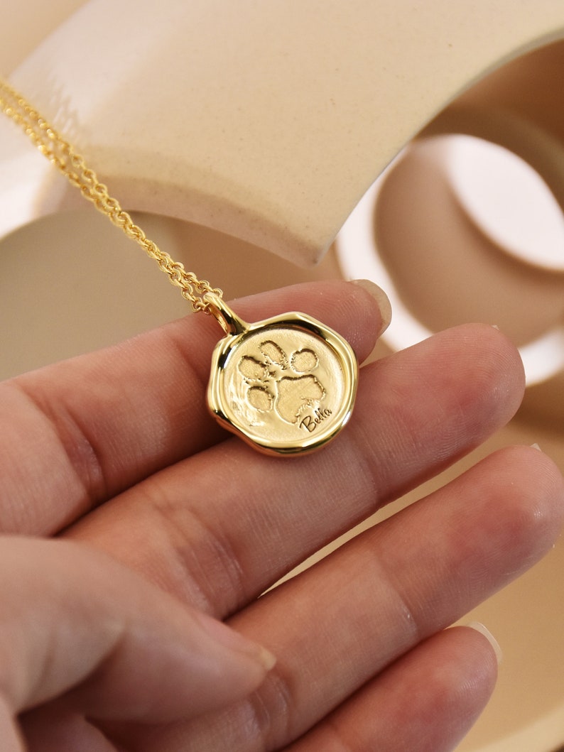 May include: Gold necklace with a paw print charm and the name "Bella" engraved on it.