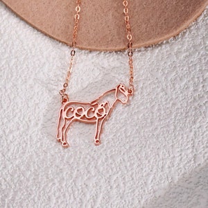 May include: A rose gold necklace with a horse silhouette pendant. The horse's outline is filled with the word "Coco".
