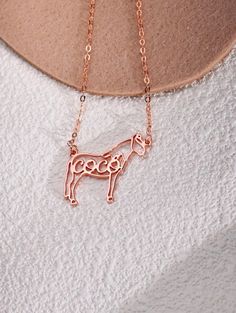 May include: A rose gold necklace with a horse silhouette pendant. The horse's outline is filled with the word "Coco".