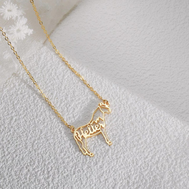 May include: A gold chain necklace with a horse pendant. The horse is made of metal and has the word "Hello" written inside its outline.