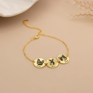 May include: A gold bracelet with three circular pendants, each displaying an engraved pet portrait. The pendants feature a dog, a rabbit, and a cat, with the names "Hugo", "Diesie", and "Sunny" inscribed below each animal illustration.
