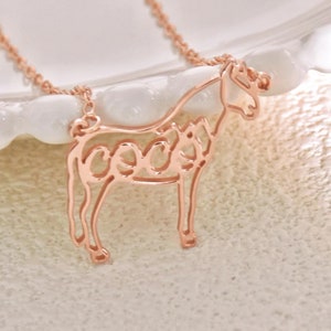 May include: A rose gold necklace with a horse pendant. The horse is outlined and the word "coco" is spelled out within the outline.