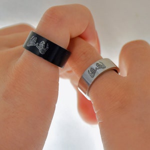 Può includere: Due anelli abbinati con un design di due mani che si tengono. Un anello è nero e l'altro è argento.