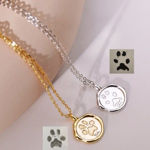 May include: Two silver and gold necklaces with paw print pendants. The pendants are engraved with the names "Bella" and "Lucy".