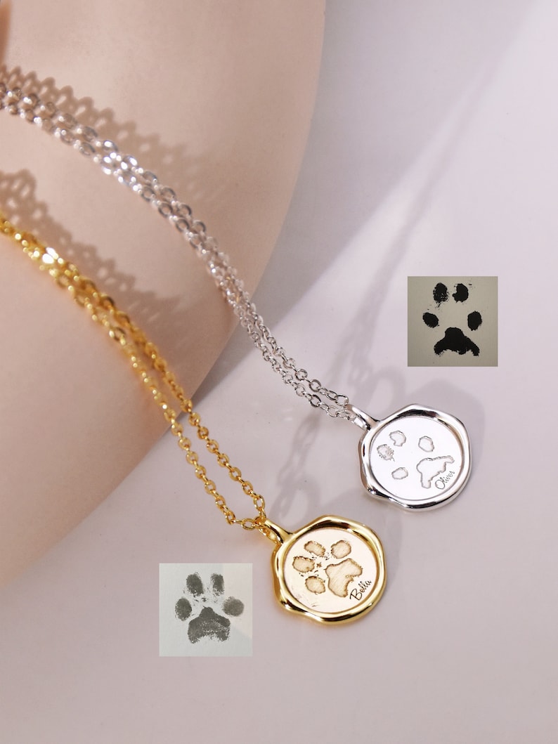 May include: Two silver and gold necklaces with paw print pendants. The pendants are engraved with the names "Bella" and "Lucy".