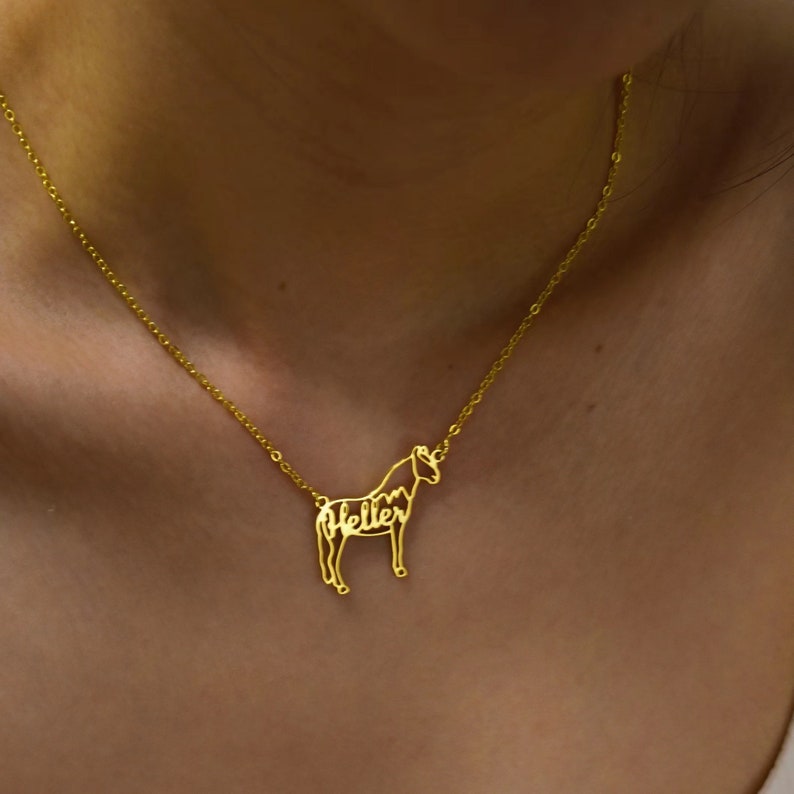 May include: A gold necklace with a horse pendant. The horse is made of metal and the name "Heller" is spelled out within the outline of the horse.