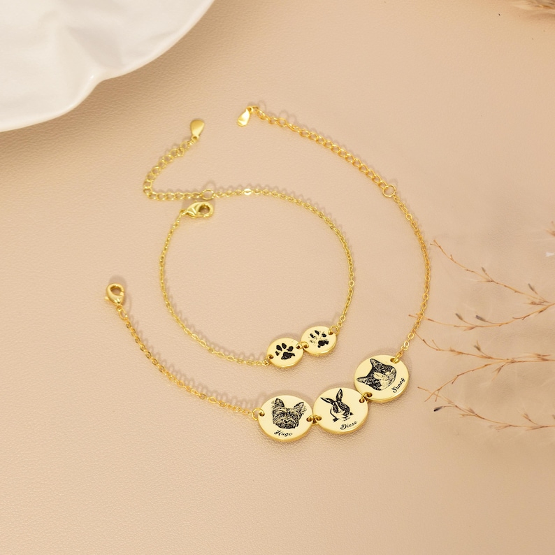 May include: Two gold-coloured bracelets. One bracelet features two circular charms with paw prints. The other bracelet has three circular charms with pet portraits and names: a dog, a rabbit, and a cat. The bracelets have adjustable chains.