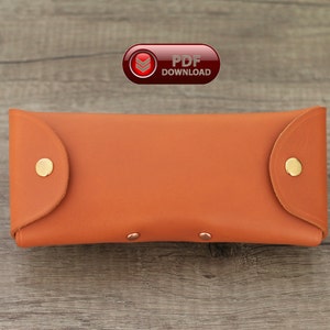Puede incluir: Un estuche para gafas de cuero naranja con cierres de bot&oacute;n a presi&oacute;n dorados. El estuche rectangular tiene bordes redondeados y una textura suave. La imagen tambi&eacute;n incluye un icono de "PDF DOWNLOAD".