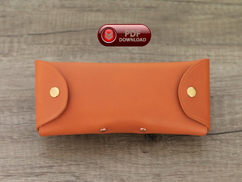 Puede incluir: Un estuche para gafas de cuero naranja con cierres de bot&oacute;n a presi&oacute;n dorados. El estuche rectangular tiene bordes redondeados y una textura suave. La imagen tambi&eacute;n incluye un icono de "PDF DOWNLOAD".