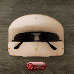 Puede incluir: Un estuche de cuero de color beige claro para gafas de sol con gafas de sol negras en el interior. El estuche est&aacute; abierto, revelando las gafas. El estuche tiene un cierre de bot&oacute;n y costuras naranjas. La imagen tambi&eacute;n incluye un bot&oacute;n rojo con el texto "PDF DOWNLOAD".