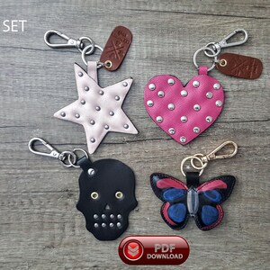 May include: Set of four leather keychains in various shapes: a star, heart, skull, and butterfly. The star is light pink, the heart is hot pink, the skull is black, and the butterfly has blue and red wings. Each keychain has silver-tone hardware.
