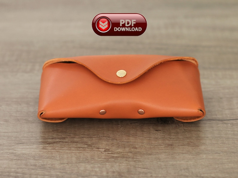 Puede incluir: Un estuche rectangular de cuero marr&oacute;n anaranjado con una solapa redondeada asegurada por un broche dorado. El estuche tiene un borde cosido y peque&ntilde;os remaches. Un bot&oacute;n de descarga PDF rojo y blanco est&aacute; en la esquina superior izquierda.