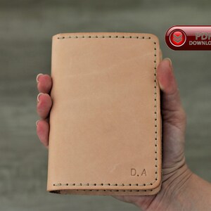 May include: A pale tan leather wallet with black stitching and the initials "D.A" embossed on the front. The wallet is held in a hand, highlighting its rectangular shape and minimalist design. A "PDF DOWNLOAD" button is visible.