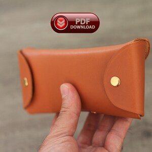 Puede incluir: Un estuche de gafas de cuero marr&oacute;n claro con forma redondeada y cierre de bot&oacute;n a presi&oacute;n. El estuche tiene herrajes met&aacute;licos dorados. La imagen incluye un bot&oacute;n "PDF DOWNLOAD".